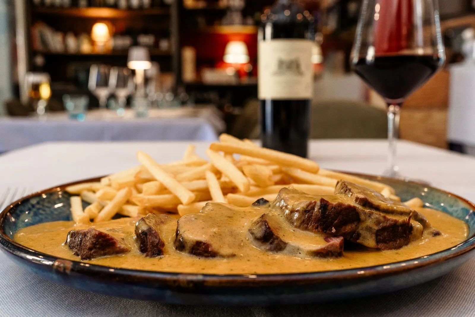 Entrecôte in salsa con patatine, una bottiglia e un calice di vino rosso