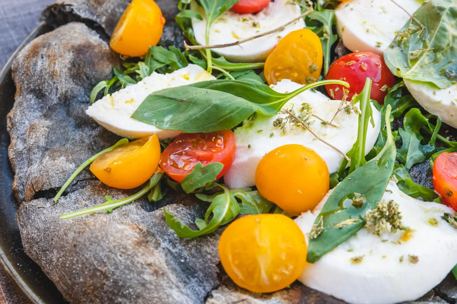 Pizza al carbone dall'impasto nero con mozzarella, pomodorini gialli e rossi e basilico